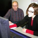 Young woman helping older man with computer